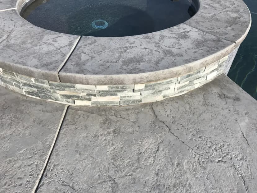 Round spa with textured concrete pool deck and stone coping
