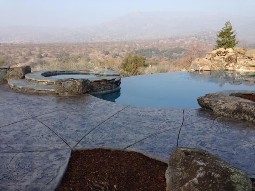 Pool deck with concrete seating and fire pit overlooking landscape
