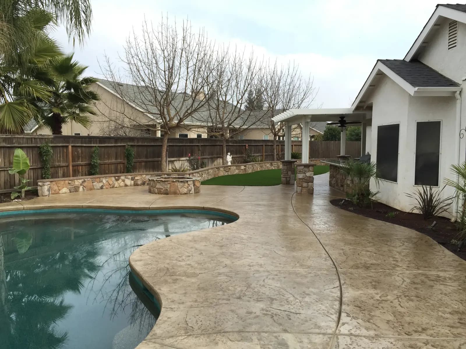 Pool deck with concrete patio, pergola structure, and fire pits