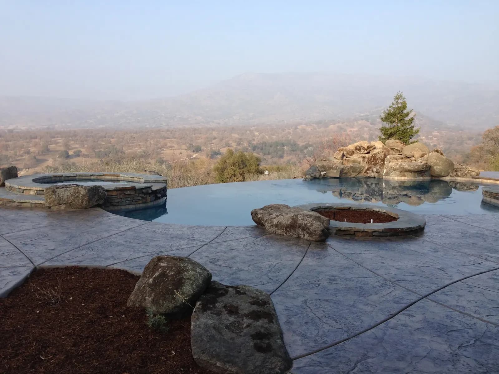 Pool deck with concrete patio and fire pit overlooking landscape