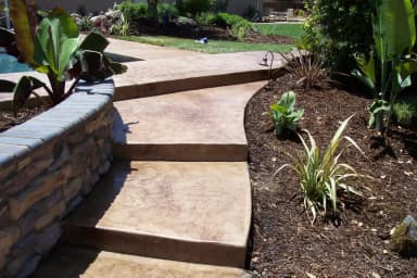 Stamped concrete patio with retaining walls and landscaping in backyard.