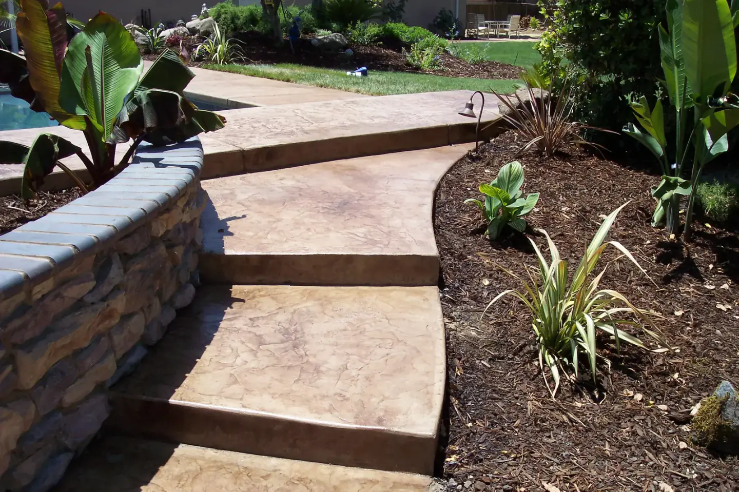 Stamped concrete patio with retaining walls and landscaping in backyard.