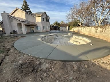 Aerial view of curved concrete patio with fire pit under construction.