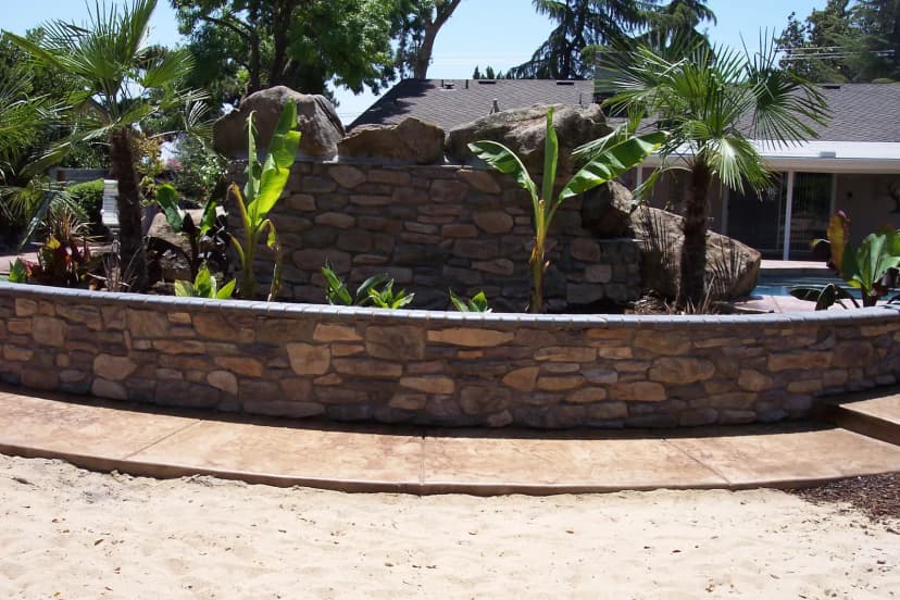 Curved stone retaining wall with concrete seating area.